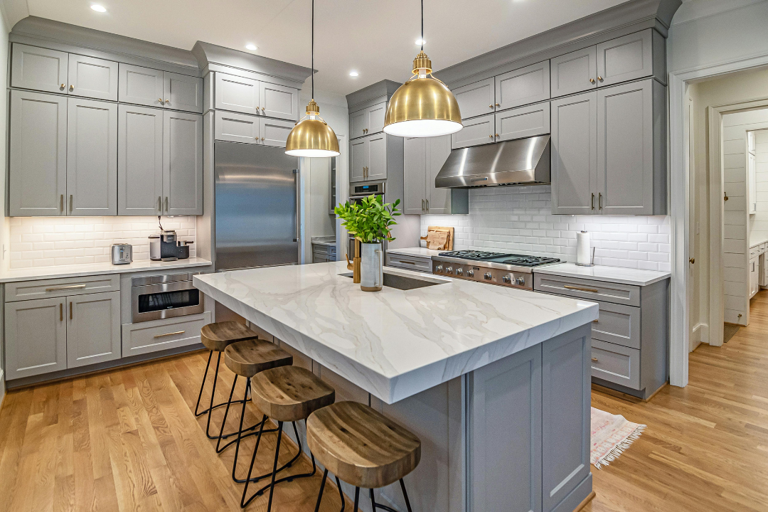 Remodeled kitchen with a marble island, custom gray cabinetry and brass pendants
